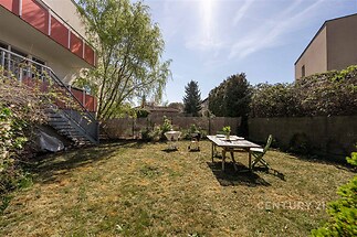 Zahrada s trávníkem a venkovním posezením, oplocená a částečně zastíněná stromem, ideální pro relaxaci nebo rodinné venkovní aktivity.