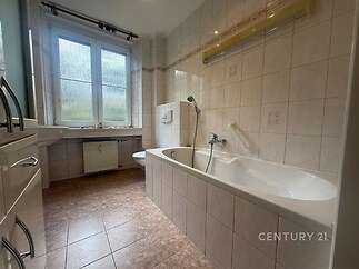 Koupelna s dlažbou a velkou vanou, vybavená umyvadlem a toaletou, disponuje velkým oknem poskytujícím přirozené světlo