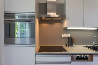 Moderní kuchyň s šedou pracovní deskou, vestavěná trouba a digestoř, indukční varná deska a nerezový dřez dodávají elegantní vzhled.