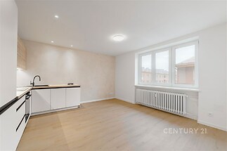 Světla kuchyň s moderními bílými skříňkami, parketová podlaha, velká okna, nově rekonstruovaný prostor.