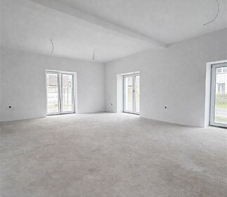 Světlý obývací pokoj s velkými okny, moderní betonová podlaha, připravený k rekonstrukci, ideální pro osobní úpravy interiéru.