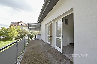 Prostorný balkon s moderním zábradlím, přístupný z místnosti s dřevěnou podlahou. Tichá lokalita s výhledem do zeleně, ideální pro relaxaci.