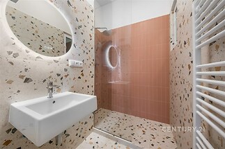 Moderní koupelna s terazzo obklady, prostorným sprchovým koutem a kulatým zrcadlem, elegantní a světlý design.