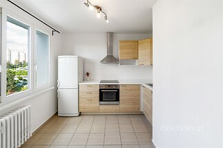 Kuchyňský kout s dlažbou, světlé dřevěné skříňky, moderní spotřebiče a velká okna poskytující dostatek přirozeného světla.