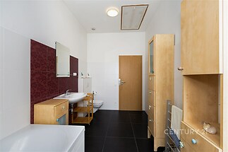 Koupelna s tmavou dlažbou, moderním vybavením, dřevěným nábytkem a bílými stěnami, prostorná s dostatkem úložných prostor.