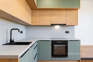 Moderní kuchyň s dřevěnými skříňkami, vestavěným spotřebičem a světlou pracovní deskou, minimalistický design a čisté linie.
