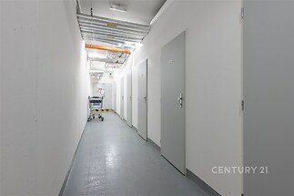 Úzká chodba s šedou podlahou, bílými stěnami a několika dveřmi. Moderní průmyslový styl, vhodné pro komerční prostory.