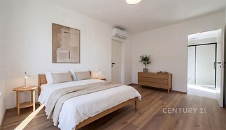 Prostorná ložnice s dřevěnou podlahou, moderní nábytek, velká okna a světlé stěny, minimalistický design, vestavěná klimatizace.