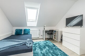 Podkrovní ložnice s laminátovou podlahou, střešním oknem a moderním nábytkem. Světlý interiér vytváří útulnou atmosféru pro relaxaci.