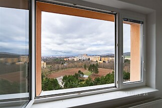 Světlý obývací pokoj s velkými okny, parketová podlaha, moderní výhled na město a zeleň, skvělá investiční příležitost.