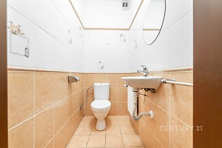 Menší koupelna s dlažbou, bílými obklady a kulatým zrcadlem, zachovalá a světlá.