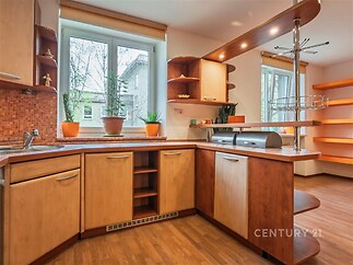 Moderní kuchyň s parketovou podlahou, velká okna, dřevěné skříňky, otevřené police, světlé prostředí.