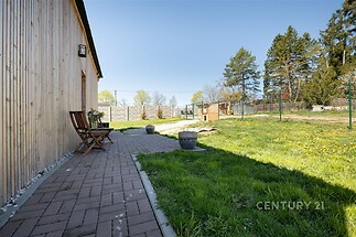 Venkovní terasa s dlažbou a dřevěným obložením, obklopená zelenou zahradou, poskytuje klidné prostředí s výhledem na stromy.