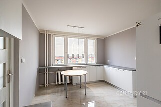 Moderní kuchyň s velkými okny, světlými skříňkami a dlažbou, nabízí prostorné uspořádání a dostatek denního světla.