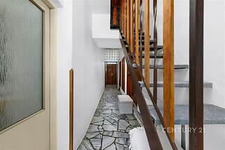 Chodba s kameninovou dlažbou, dřevěným zábradlím a vstupními dveřmi. Funkční design a přírodní materiály přinášejí moderní pocit.