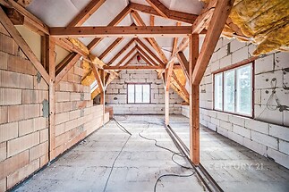 Podkrovní místnost ve výstavbě, dřevěné trámy, velká okna, příprava pro elektřinu, světlý prostor, cihlové a betonové zdi.