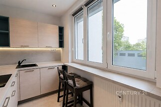 Moderní kuchyň s velkými okny, světlým dřevěným nábytkem a vestavěnými spotřebiči, nabízí elegantní a světlé prostředí pro vaření.