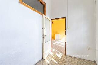 Vstupní hala s dlažbou, vysoké stropy a dveře vedou do světlé místnosti s velkými okny, ideální pro moderní rekonstrukci.