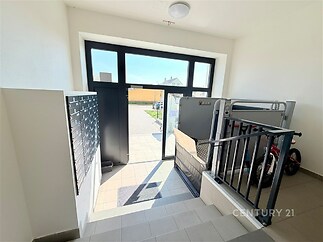 Vstupní hala bytového domu s dlažbou a velkými okny, umožňujícími přirozené světlo, vybavená moderními poštovními schránkami.