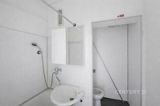 Jednoduchá koupelna s bílými dlaždicemi a umyvadlem, sprchou a zrcadlovou skříňkou, čistý a praktický prostor vhodný k úpravám.