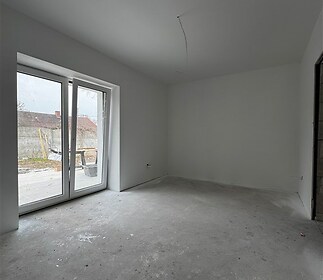 Světlý obývací pokoj s velkými okny a betonovou podlahou, připravený k dokončení, nabízí moderní možnosti úprav pro budoucí majitele