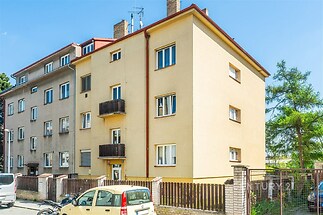 Exteriér bytového domu s novou fasádou, velkými okny a klasickým stylem nabízí ideální městské bydlení ve strategické lokalitě.