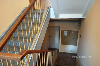 Schodiště s dřevěným zábradlím, dlažba na podlaze, světlé stěny. Prostor ideální k renovaci v činžovním domě.