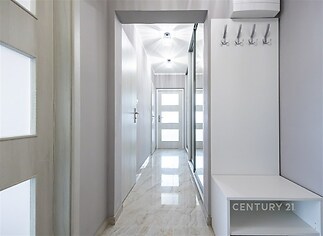 Úzká předsíň s moderní dlažbou, světlými stěnami a velkým zrcadlem. Praktický věšák na kabáty přidává funkčnost.