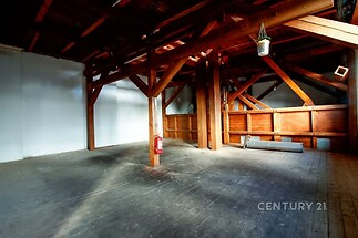 Podkrovní prostor s dřevěnými trámy a parketovou podlahou, ideální pro přestavbu. Velká okna zajišťují dostatek světla, prostor je připraven k rekonstrukci.