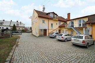 Dvůr s parkováním a vjezdovou bránou, vydlážděná cesta, přilehlé budovy s balkony, venkovní schodiště, moderní vzhled budovy.
