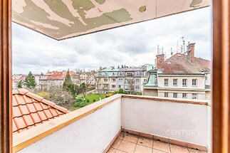 Výhled z balkónu s dlažbou a rustikálním zábradlím, nabízející pohled na klidnou rezidenční čtvrť s upravenými střechami a zahradami.