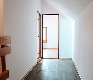Chodba s tmavou dřevěnou podlahou, světlé stěny a velké okno vpředu, moderní a světlý prostor.