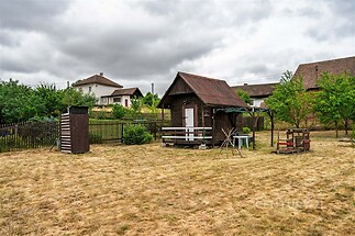 Zahrada s dřevěnými zahradními domky, obklopená plotem, s několika mladými stromy a suchým travnatým povrchem, vhodná pro rekreační účely.