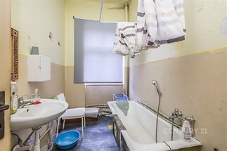 Koupelna s vanou, umyvadlem a žaluziemi. Omítka na stěnách potřebuje renovaci, podlaha je betonová. Celkově původní stav.