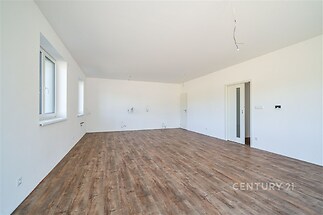 Prostorný obývací pokoj s parketovou podlahou, velká okna zajišťují dostatek světla, moderní minimalistický design v neutrálních barvách.