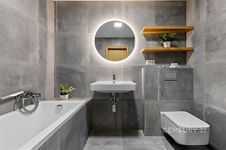 Moderní koupelna s dlažbou a velkým zrcadlem, kombinovaná vana a sprcha, plovoucí police s dekoracemi, elegantní designový prvek.