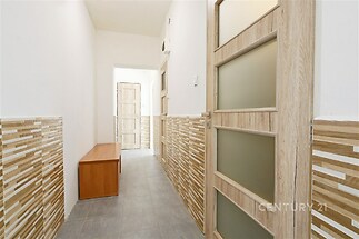 Úzká chodba s dlažbou a dřevěnými obklady, prosvětlená dveřmi s matným sklem, moderní design v rekonstruovaném bytě.