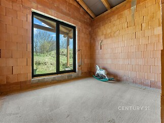 Hrubá nedokončená místnost s velkými okny a betonovou podlahou, nabízí potenciál pro světlý a moderní interiér v přírodním prostředí