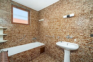 Koupelna s vintage dlažbou, vanou a umyvadlem. Menší okno umožňuje přirozené světlo. Vhodné k rekonstrukci.