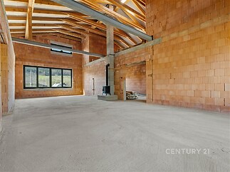 Prostorný obývací pokoj, betonová podlaha, krbová kamna, nedokončená stavba, moderní design, vysoké stropy, velká okna.