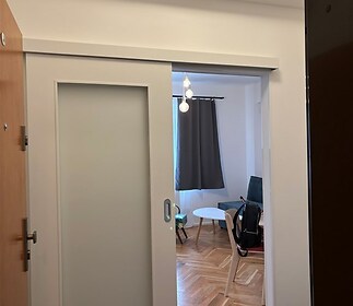 Vstupní hala s parketovou podlahou, posuvnými dveřmi a moderním osvětlením, vedoucí do světlého obývacího pokoje.