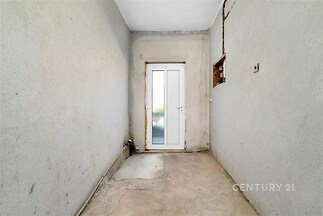 Úzký prostor s betonovou podlahou, prosklené dveře vedoucí ven, nezrekonstruovaný stav, vhodný pro úložný prostor nebo technickou místnost.