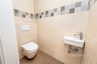 Toaleta s moderní dlažbou, světlé obklady a úsporné závěsné WC, kompaktní umyvadlo, čistý a udržovaný vzhled.