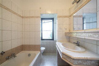 Koupelna s dlažbou, světlá místnost, velké zrcadlo a vana; nabízí praktické uspořádání a funkční keramické obklady.