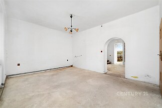 Prázdný obývací pokoj s neutrálními bílými stěnami, podlahou připravenou k úpravě a arkýřem. Interiér vhodný k rekonstrukci.