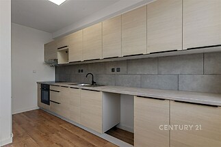 Moderní kuchyň s parketovou podlahou, světlými dřevěnými skříňkami a elektrickou troubou, šedá dlažba na stěně dodává elegantní vzhled.