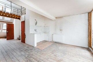 Prázdná kuchyň s dřevěnou podlahou, bílými stěnami a velkými okny, ideální pro rekonstrukci v moderním stylu.