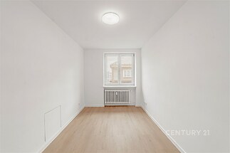 Světlý pokoj s parketovou podlahou, bílými stěnami a velkým oknem, které dodává moderní a čistý vzhled.