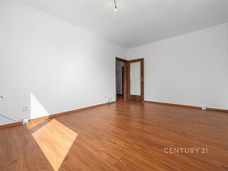 Světlý obývací pokoj s dřevěnou podlahou, velkými okny pro přirozené světlo a moderním minimalistickým stylem.