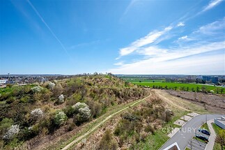 Výhled z balkónu na zelenou krajinu a parkoviště, klidná lokalita, ideální pro milovníky přírody a relaxaci, panorama s modrou oblohou.